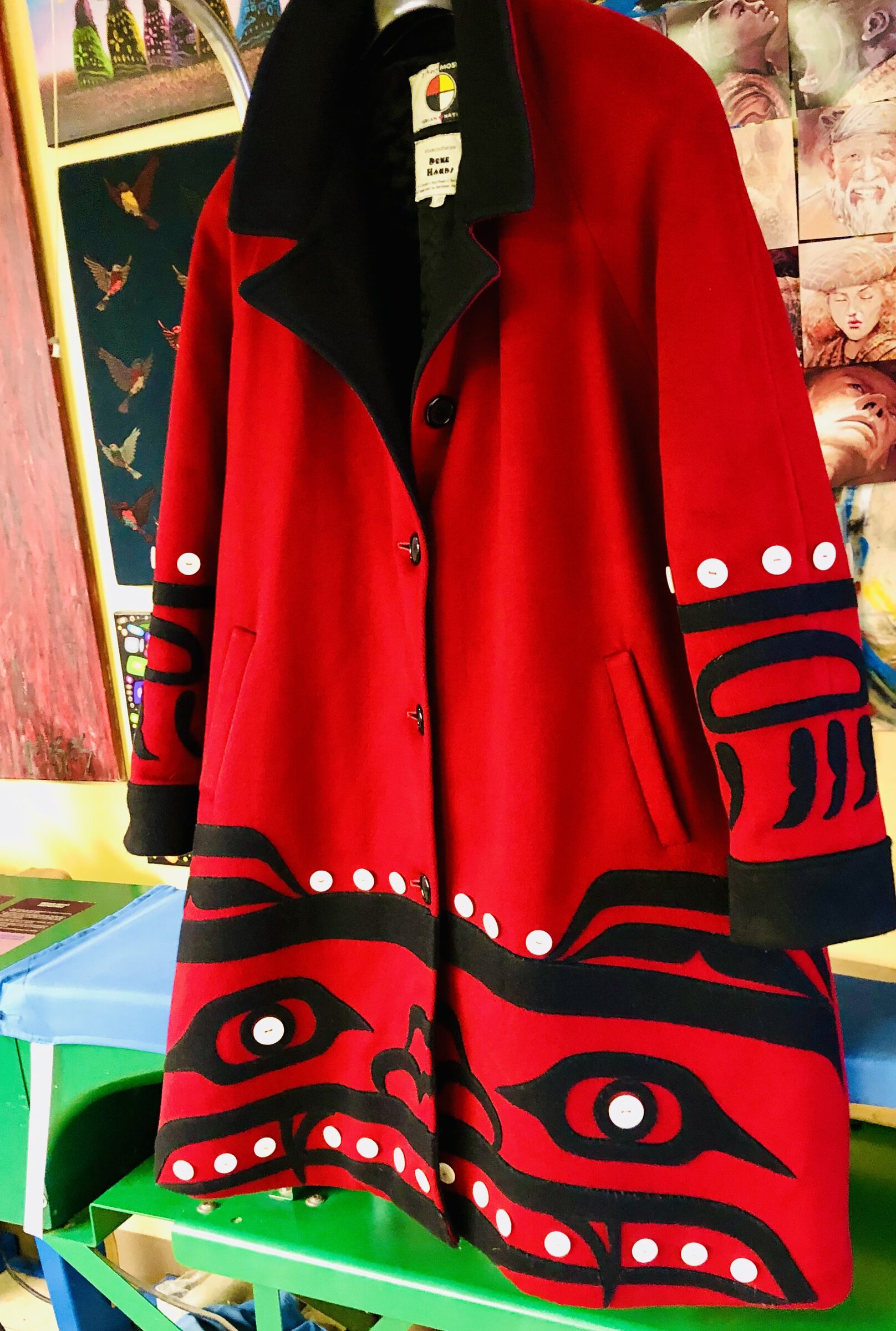 Bright red coat with black formline graphics, hanging over the work table