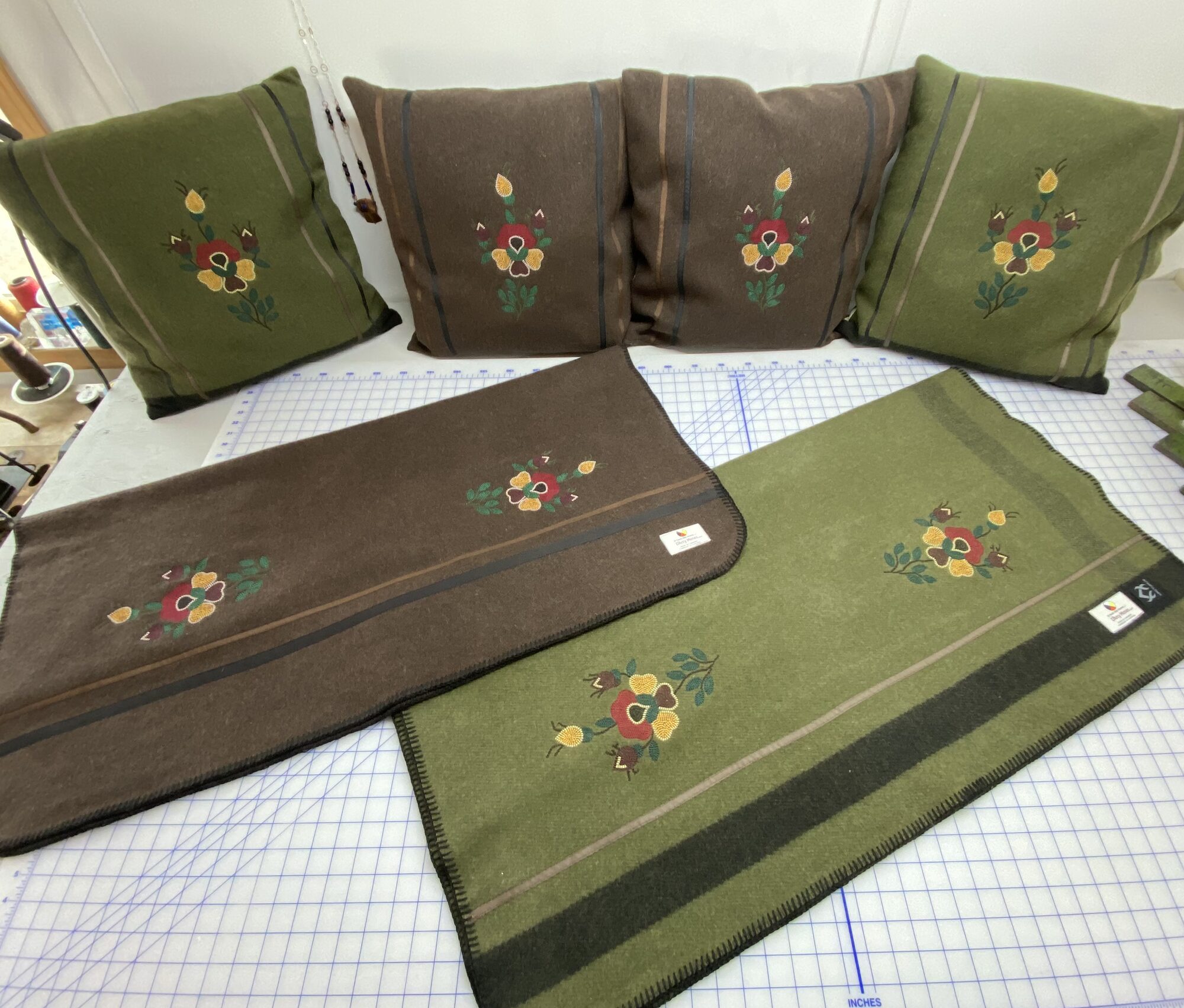Olive and brown wool pillows and runners with floral embroidery on a cutting table.